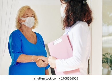 Senior Woman In Medical Mask Greeting Doctor Visiting Her At Home