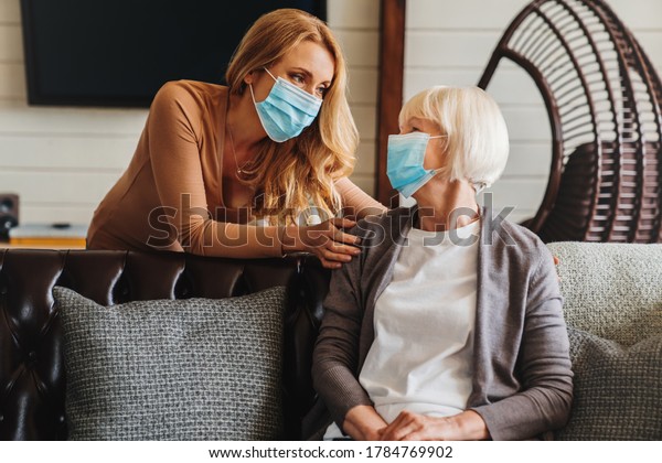 Senior woman in medical mask with social worker
visiting her at home