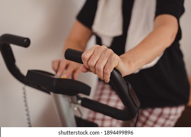 Senior Woman In Mid 70's Exercise On Stationary Bike At Home. Active Mature Female Checking Parameters During Cycling Workout. 