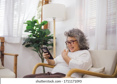 Senior Woman Old Sitting On Couch Using Smartphone Browsing, Online Shopping Or Video Call Chat With Family. Stay Safe At Home Preventing Coronavirus Outbreak Crisis. Aged People Connecting Technology