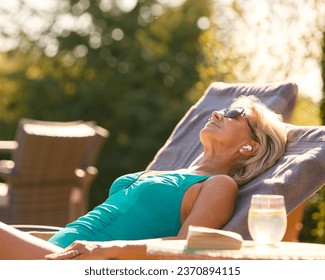 Senior Woman On Holiday In Swimming Costume Wearing Wireless Earbuds By Hotel Swimming Pool - Powered by Shutterstock