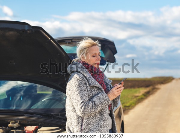 Senior woman on the road having problem with\
a car, she is calling for\
assistance.
