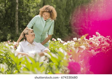 Senior woman on a wheelchair and looking at her young nurse, surrounded by flowers - Shutterstock ID 674330680