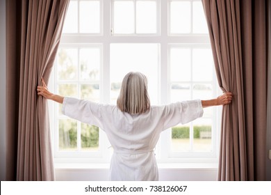 Senior Woman Opening Bedroom Curtains And Looking Out Of Window - Powered by Shutterstock