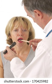 Senior Woman Opening Her Mouth For The Doctor To Look Inside With Tongue Depressor  And Light 