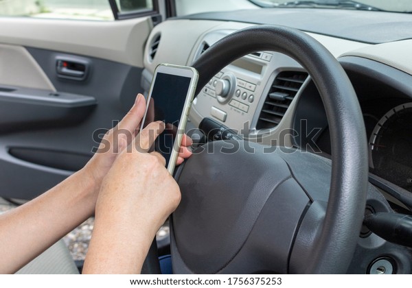 Senior woman operating a smartphone in the\
driver\'s seat while\
parked