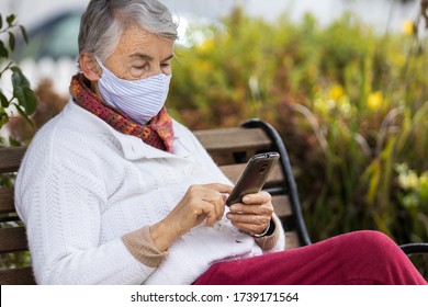 Senior woman outdoors using her cell phone wearing a home made face mask during the coronavirus quarantine de-escalation - Powered by Shutterstock