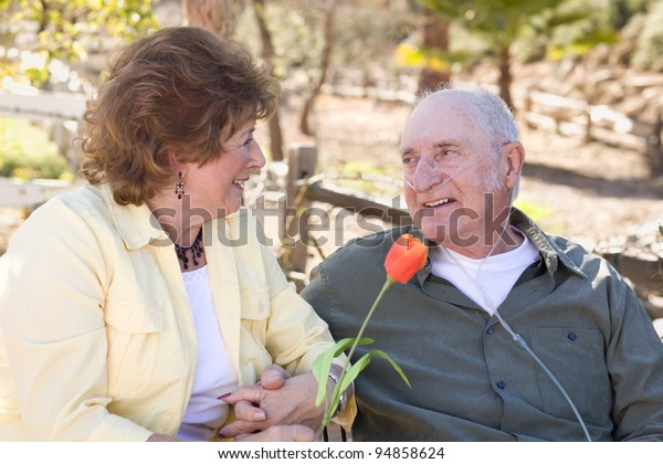 Senior Woman Outside with Seated Man Wearing\
Oxygen Tubes.