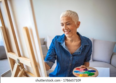 Senior woman painting at home  Happy elderly woman looking at her painting at home  Happy retired woman painting canvas for fun at home  Portrait Of Senior Female Artist Working On Painting