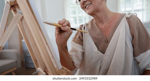 Senior Woman Painting on Canvas at Home in Bright Room with Natural Light - Powered by Shutterstock