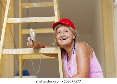 Senior Woman Painting Wall In New House. She Is Using Ladder.