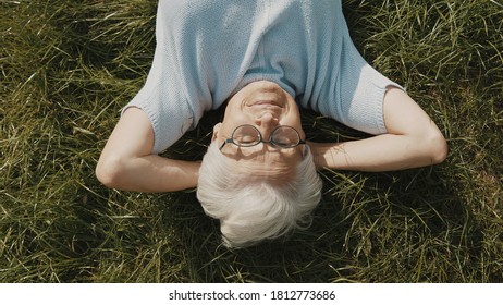 Senior Woman, Pensioner Lying On The Grass With Hands Under Her Head. Overhead Close Up Shot. High Quality Photo