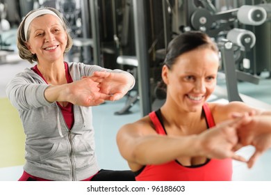 Senior Woman With Personal Fitness Trainer Stretch Out At Gym