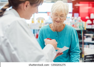 Senior Woman In Pharmacy Talking To The Chemist Or Pharmacist Explain Effects Of A Drug