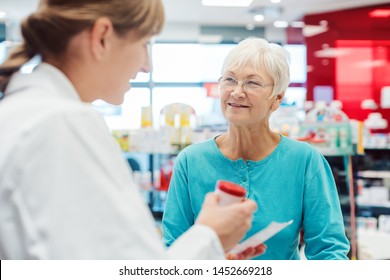 Senior Woman In Pharmacy Talking To The Chemist Or Pharmacist Explain Effects Of A Drug