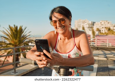 Senior woman, phone and scooter of a person on holiday in Florida feeling happiness in the sun. Social media scroll, text and travel of a elderly female on 5g mobile connection with smile in summer - Powered by Shutterstock