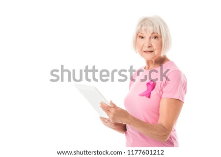 senior woman in pink t-shirt with breast cancer awareness ribbon using digital tablet and looking at camera isolated on white 
