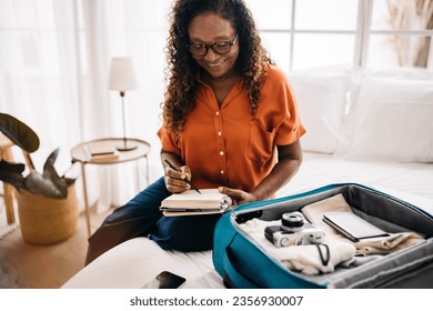 Senior woman planning a vacation with a checklist list, ticking off travel essentials she has packed into her luggage. Woman looking excited to relax, unwind, and have some fun on her holiday. - Powered by Shutterstock