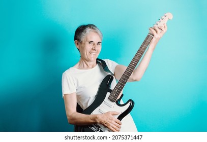 Senior Woman Playing Electric Guitar.Close Up Portrait Of Beautiful Old Woman Playing Electric Guitar On A Blue Background. Learning New Hobbies.