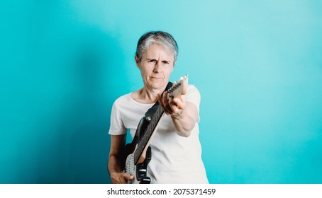 Senior Woman Playing Electric Guitar.Close Up Portrait Of Beautiful Old Woman Playing Electric Guitar On A Blue Background. Learning New Hobbies.