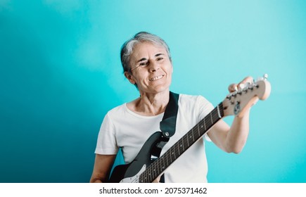 Senior Woman Playing Electric Guitar.Close Up Portrait Of Beautiful Old Woman Playing Electric Guitar On A Blue Background. Learning New Hobbies.