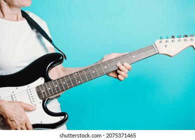 Senior Woman Playing Electric Guitar.Close Up Portrait Of Beautiful Old Woman Playing Electric Guitar On A Blue Background. Learning New Hobbies.