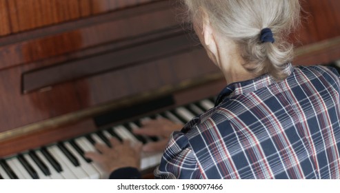 Senior woman is playing the piano. Back view.