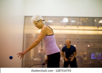 Senior woman playing squash with a mid-adult man.