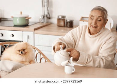 Senior woman with Pomeranian dog pouring tea at table in kitchen - Powered by Shutterstock