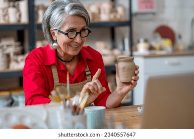 Senior woman potter broadcasting live lesson masterclass painting clay products, teaching students online. - Powered by Shutterstock