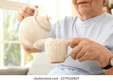 Senior woman pouring tea into cup at home, closeup - Powered by Shutterstock