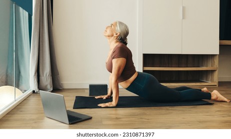 Senior woman practices upward facing dog pose on her fitness mat, feeling the strength and flexibility in her body. Mature woman finding focus and balance in her home yoga routine. - Powered by Shutterstock