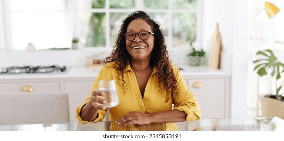 Senior woman practicing a healthy lifestyle, keeping herself hydrated by drinking plenty of water at home. Happy mature woman taking care of her health and well-being as she ages. - Powered by Shutterstock