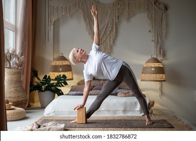 Senior woman practicing yoga, stretching in Utthita Trikonasana exercise, extended triangle pose, working out at home.