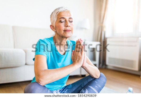 Senior woman in the prayer position . Woman\
practicing yoga, relaxing in prayer position on mat, Padmasana\
exercise, elderly woman wearing sportswear working out, meditating\
in yoga studio or at\
home