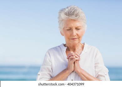 Senior woman praying on the beach on a sunny day - Powered by Shutterstock