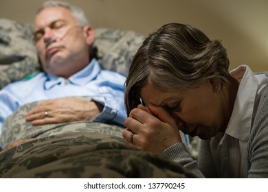 Senior Woman Praying For Sick Man Sleeping In Hospital Bed