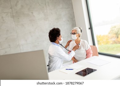 Senior Woman With Protective Facial Mask Having A Medical Exam By Black Female Doctor In The Office