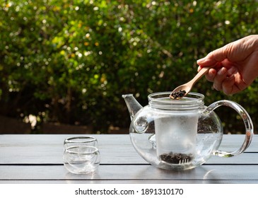 senior woman put dry tea leaves into glass kettle to make afternoon tea in garden - Powered by Shutterstock