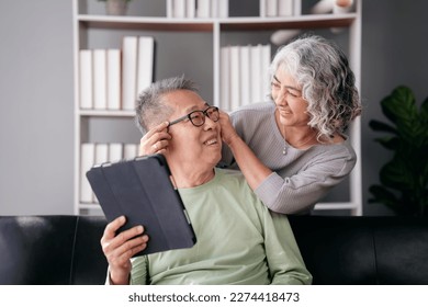 Senior woman putting glasses on beloved while sitting on the couch to watching movie on tablet and spending time to doing activity for relaxation in life retirement together at living room of home.