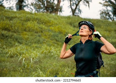 Senior Woman Putting On Her Sports Helmet Get Ready For The Exercising Extreme Sport Outdoors In Green Nature. Copy Space