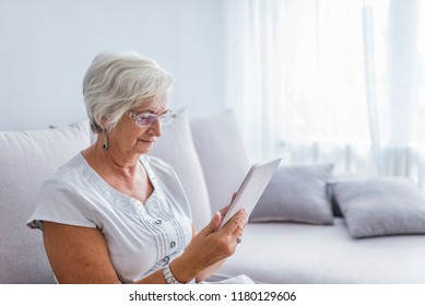 Senior woman reading a message, e-book or information on her tablet computer with a look of excited anticipation as she sits on a couch at home.Discovering the wonders of the web - Powered by Shutterstock