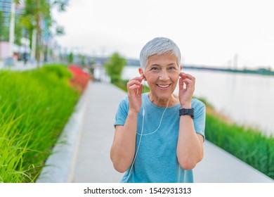 Senior woman relaxing after exercising. Portrait of senior woman adjusting earphones before exercising. fitness, sport and healthy lifestyle concept - senior woman with earphones at summer park - Powered by Shutterstock