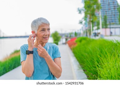 Senior woman relaxing after exercising. Portrait of senior woman adjusting earphones before exercising. fitness, sport and healthy lifestyle concept - senior woman with earphones at summer park - Powered by Shutterstock