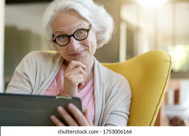 Senior woman relaxing in armchair and using digital tablet - Shutterstock ID 1753006166