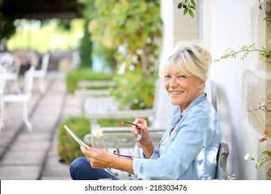 Senior woman relaxing outside and using tablet - Powered by Shutterstock