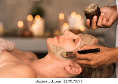 Senior woman relaxing while beautician getting purifying clay mask on her face. Closeup hand of masseuse applying mud on face of mature lady in spa center. Anti aging facial treatment with brush. - Powered by Shutterstock