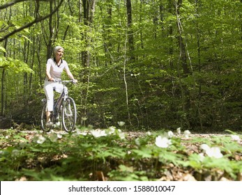 Senior woman riding bicycle on wooded road - Powered by Shutterstock