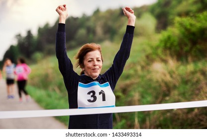 Senior woman runner crossing finish line in a race competition in nature. - Powered by Shutterstock