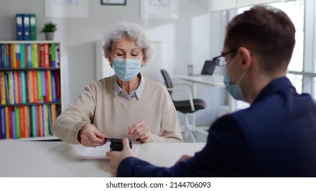 Senior Woman In Safety Mask Pay For Education Courses In Modern Department. Insurance Agent In Mask Give Aged Client Contract And Receive Online Payment